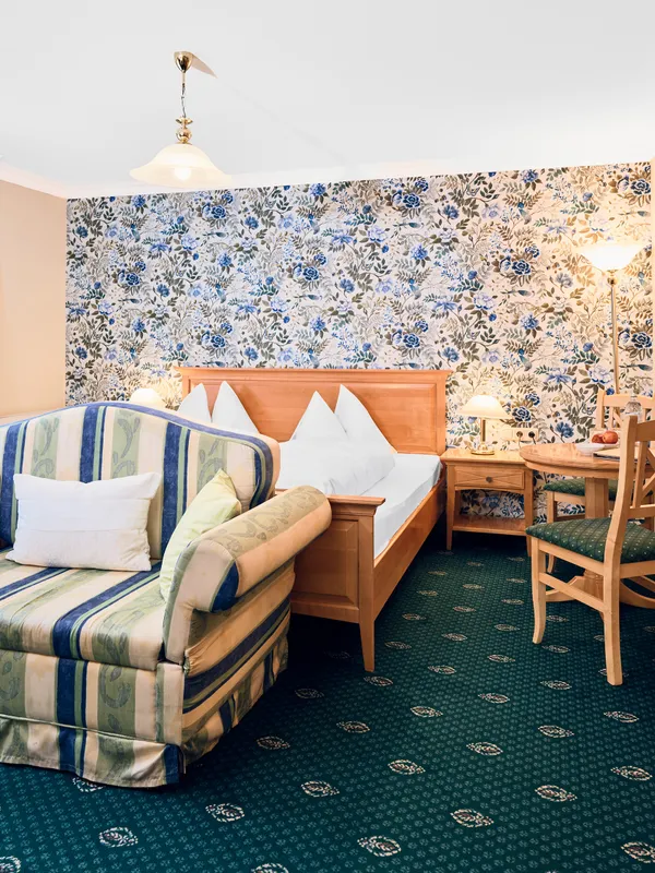 Cozy hotel room with floral wallpaper, striped loveseat, wooden furniture, and double bed